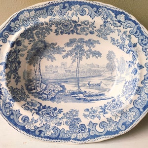 Könnte beinhalten: Ovale Servierplatte mit blau-weißem Transferdruck. Die Mitte zeigt eine Landschaft mit Bäumen, einem Fluss und einem Schloss. Der Rand ist mit floralen und Scroll-Mustern verziert. Ein klassisches Stück Vintage-Geschirr.