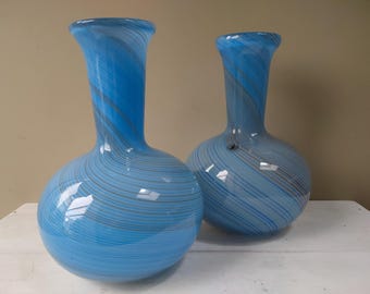 May include: Two blue glass vases with a swirling white and gray pattern. The vases have a round body and a narrow neck.