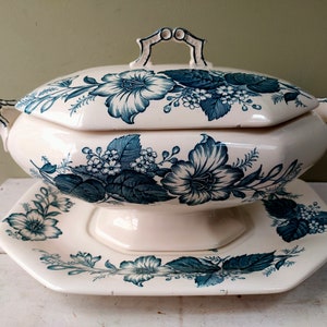 May include: Cream ceramic soup tureen with a matching lid and serving platter. The tureen and platter are decorated with a blue floral pattern. The tureen has a handle on the lid and two side handles.
