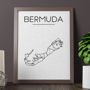 May include: Framed print featuring a minimalist map of Bermuda in black lines on a white background. The word "BERMUDA" is printed in a bold, sans-serif font above the map. The frame is a dark brown color.