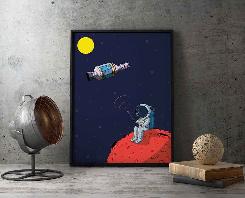 Puede incluir: Impresi&oacute;n art&iacute;stica enmarcada que representa a un astronauta sentado en un planeta rojo, sosteniendo un mando a distancia, con un sat&eacute;lite en el espacio y una luna amarilla. La obra es de estilo cartoon sobre fondo azul oscuro.