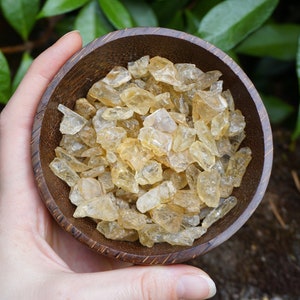 May include: A small wooden bowl filled with golden citrine crystals. The bowl is held in a person's hand.