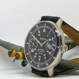 May include: A silver-cased wristwatch with a black face and white numerals, featuring a leather band. The watch is displayed on a small, olive-green model airplane with yellow accents. The watch face includes the text "SPECIAL FOR NAVIGATOR".