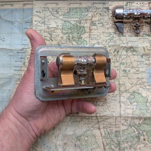 Puede incluir: Primer plano de un zócalo de tubo de radio vintage con dos tubos insertados. El zócalo está hecho de metal y tiene un acabado plateado. Los tubos son de vidrio y tienen un acabado transparente. El zócalo está montado en un mapa.