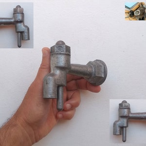 Puede incluir: Un grifo de metal plateado con una manija redonda y un caño. El grifo está sujeto a una pared.