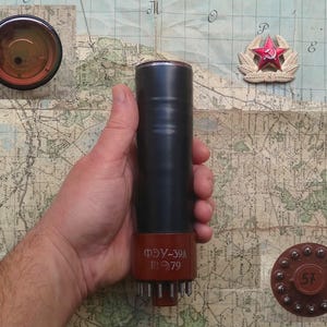 May include: A black vacuum tube with a red label that reads "ФЭУ-39А П1079". The tube is being held in a hand against a map background.