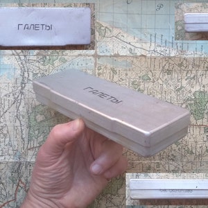 May include: A silver metal box with the word "ГАЛЕТЫ" printed on the top and bottom. The box is approximately 25 cm long and 5 cm wide.