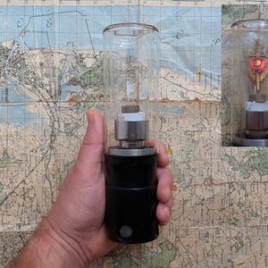 May include: A vintage black and silver lamp with a clear glass cylinder. The lamp features a cylindrical base and a metal top. The background is a map.