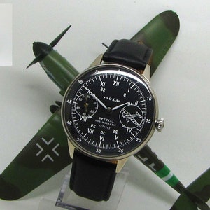 May include: A black-faced Doxa Special watch with a black leather band, displayed on a model airplane. The watch has white numerals and hands. A small figurine of a pilot stands nearby. The airplane is green and brown.
