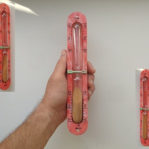 May include: A pink hourglass timer with a clear glass bulb and a brown sand inside. The timer is marked with numbers from 0 to 10 and the word "MINUTES".