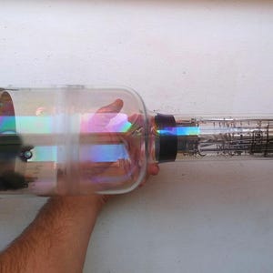 May include: A large, clear glass vacuum tube with a metal base and a black band around the middle. The tube is about 12 inches long and has a iridescent coating on the glass.