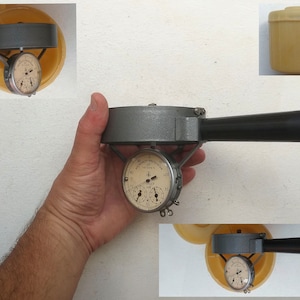 Może przedstawiać: Szary metalowy przyrząd z czarnym uchwytem i dwoma analogowymi wskaźnikami. Wskaźniki mają białe tarcze z czarnymi oznaczeniami i czarnymi wskazówkami. Urządzenie jest trzymane w dłoni.