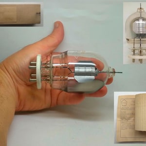 Pode incluir: Um tubo de vácuo de vidro transparente com uma grade de metal no seu interior. O tubo é segurado na mão e tem uma base de cerâmica branca com cinco pinos. O tubo está etiquetado como "6E5P".