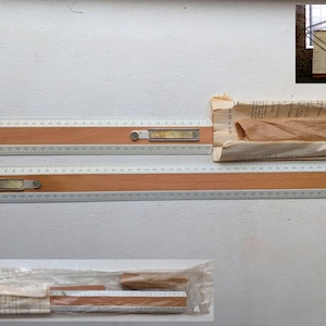 May include: Two wooden and plastic drafting rulers with metal accents. One ruler is partially open, revealing a metal protractor. The rulers are on a white surface, with a rolled-up paper document.