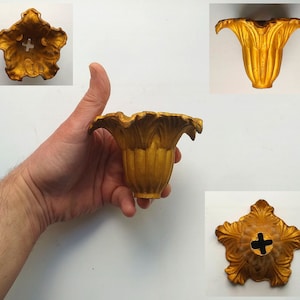 Op de afbeelding: Gouden metalen lampenkap met een decoratief, bloemvormig ontwerp. De kap heeft een gat in het midden om aan een lamp te bevestigen.