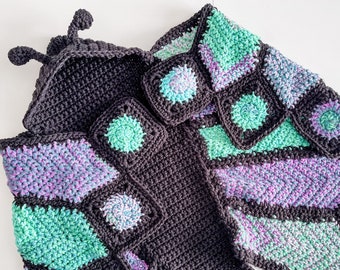 May include: A black crocheted butterfly hooded blanket with green and purple accents. The blanket is made with a variety of stitches and textures.