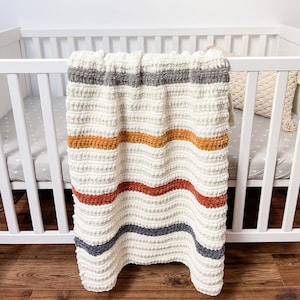 May include: A white knitted baby blanket with stripes of gray, orange, and red.