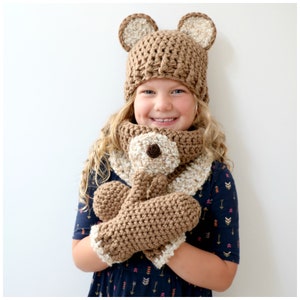 Peut inclure: Un ensemble de bonnet, écharpe et mitaines en crochet marron en forme d'ours. Le bonnet a des oreilles d'ours et l'écharpe a un visage d'ours.