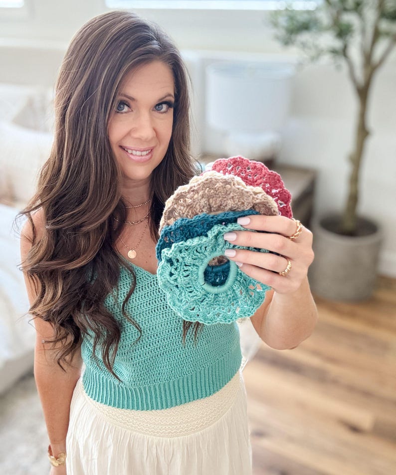 May include: A collection of handmade crochet scrunchies in various colors, including teal, brown, and red. The scrunchies are displayed against a soft background, showcasing their textured, detailed design. These hair accessories are perfect for adding a touch of handmade charm to any hairstyle.