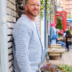 May include: A light blue crochet cardigan with wooden buttons. The open-front sweater has a textured knit pattern and is worn over a white t-shirt. The cardigan is a casual, comfortable style.