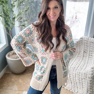 May include: A cream-coloured crochet cardigan with a granny square pattern in shades of pink, blue, and green. The cardigan has a long, open front and long sleeves.