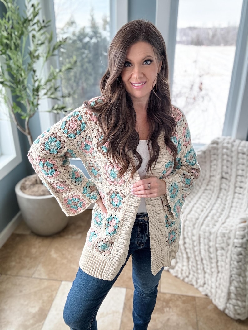 May include: A cream-coloured crochet cardigan with a granny square pattern in shades of pink, blue, and green. The cardigan has a long, open front and long sleeves.