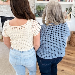 May include: Two women wearing handmade crochet tops. One top is cream-colored, the other is light blue. Both tops have a square neckline and short sleeves. The women are wearing jeans. The background includes a fireplace, shelves, and a wooden floor.