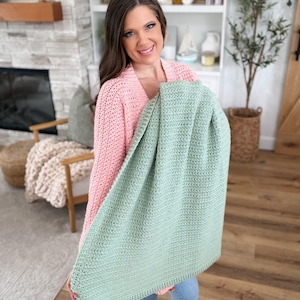 Puede incluir: Una manta rectangular de ganchillo en color verde salvia que presenta un patr&oacute;n de puntos texturizados consistente en toda su superficie. La manta est&aacute; elaborada con un hilo de grosor uniforme y muestra un aspecto tejido denso con un borde simple.
