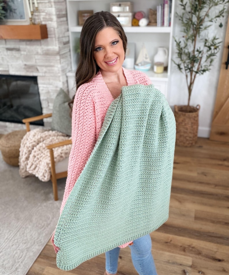 Puede incluir: Una manta rectangular de ganchillo en color verde salvia que presenta un patr&oacute;n de puntos texturizados consistente en toda su superficie. La manta est&aacute; elaborada con un hilo de grosor uniforme y muestra un aspecto tejido denso con un borde simple.