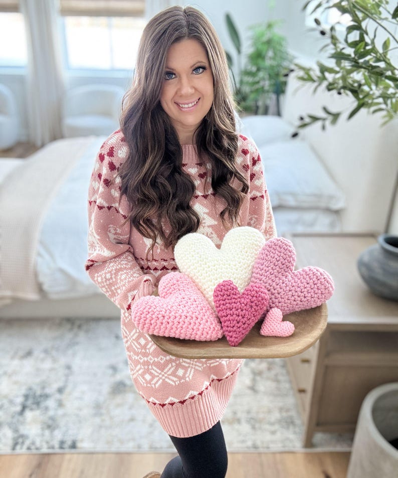 Pu&ograve; includere: Una collezione di cinque cuori all'uncinetto in varie tonalit&agrave; di rosa e bianco. I cuori sono disposti su un vassoio di servizio in legno.