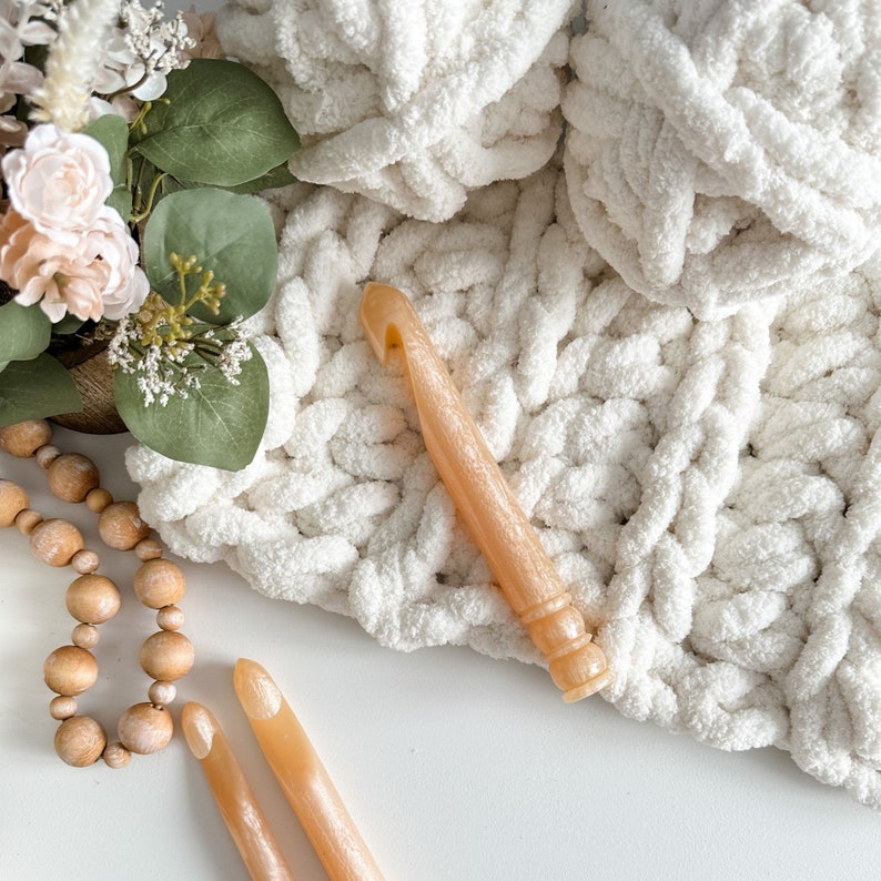 Peut inclure: Deux crochets en bois pour le crochet, l'un avec une extr&eacute;mit&eacute; pointue et l'autre avec un crochet, sont pos&eacute;s sur une surface blanche. Une couverture blanche et moelleuse est en arri&egrave;re-plan.