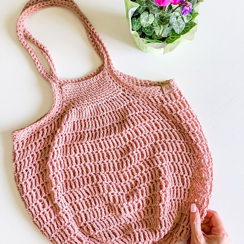 May include: A pink crocheted tote bag with a brown leather tag that says "M&H".
