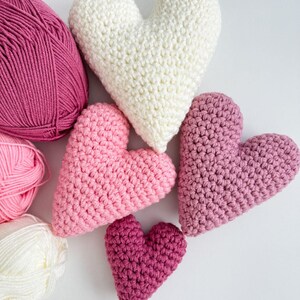 Pu&ograve; includere: Cinque cuori all'uncinetto in varie tonalit&agrave; di rosa e bianco. I cuori sono disposti in un gruppo, con il cuore pi&ugrave; grande al centro e il cuore pi&ugrave; piccolo in basso.