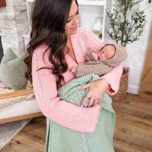 Puede incluir: Un c&aacute;rdigan de ganchillo rosa claro de manga larga con cuello en V, una manta de ganchillo verde claro y un conjunto de ganchillo beige para beb&eacute; que incluye gorro y su&eacute;ter. Las prendas presentan un patr&oacute;n de punto texturizado uniforme.