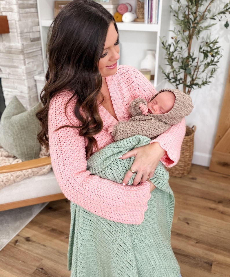 Puede incluir: Un c&aacute;rdigan de ganchillo rosa claro de manga larga con cuello en V, una manta de ganchillo verde claro y un conjunto de ganchillo beige para beb&eacute; que incluye gorro y su&eacute;ter. Las prendas presentan un patr&oacute;n de punto texturizado uniforme.