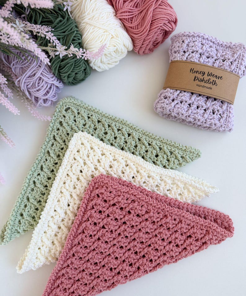 Puede incluir: Pa&ntilde;os de cocina de ganchillo hechos a mano en tonos rosa, crema y verde, junto con ovillos de lana a juego. Un pa&ntilde;o de cocina est&aacute; envuelto con una banda de papel marr&oacute;n que dice "Honey Weave Dishcloth Handmade".