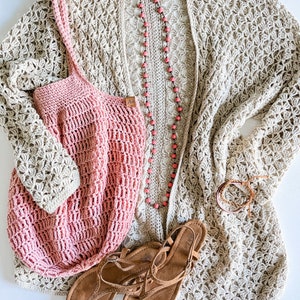 May include: A beige crochet cardigan with a pink crochet tote bag and brown sandals. The cardigan has a delicate floral pattern and the tote bag has a simple grid pattern. The sandals have a strap across the foot and an ankle strap.