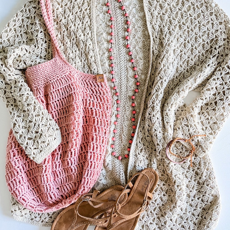 May include: A beige crochet cardigan with a pink crochet tote bag and brown sandals. The cardigan has a delicate floral pattern and the tote bag has a simple grid pattern. The sandals have a strap across the foot and an ankle strap.