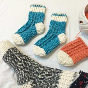 May include: Three pairs of knitted socks in different colors and patterns. One pair is blue and white, another is orange and white, and the third is gray and white.