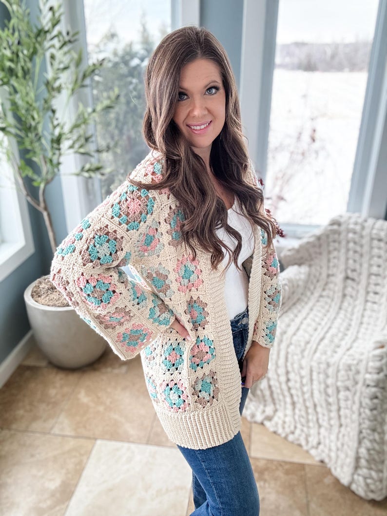 May include: A crocheted cardigan with a granny square pattern in shades of beige, pink, and blue. The cardigan has a long, open front and long sleeves.