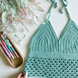 May include: A teal crochet halter top with a delicate, open-stitch pattern. The top has a V-neckline and adjustable straps.