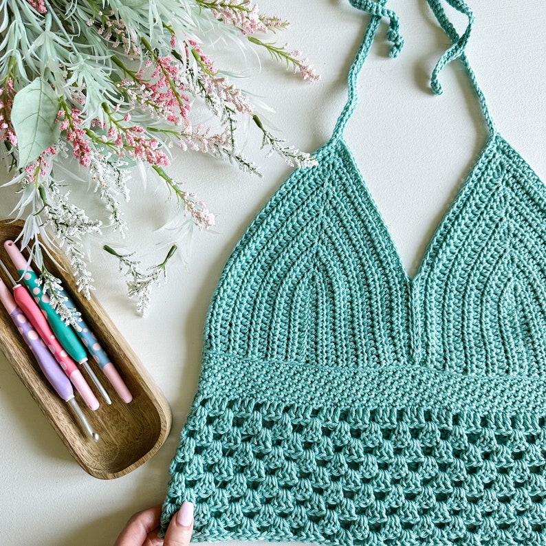 May include: A teal crochet halter top with a delicate, open-stitch pattern. The top has a V-neckline and adjustable straps.