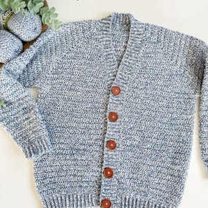 May include: A blue and white speckled knit cardigan with a V-neck and long sleeves. The sweater has five brown buttons down the front. The knitwear is displayed on a white surface.
