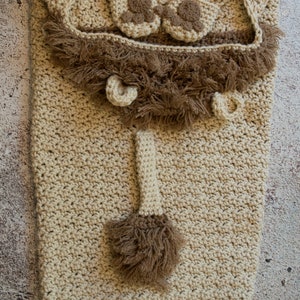 May include: A crocheted lion costume for a baby, featuring a hooded blanket, booties, and a tail with a brown fur trim.