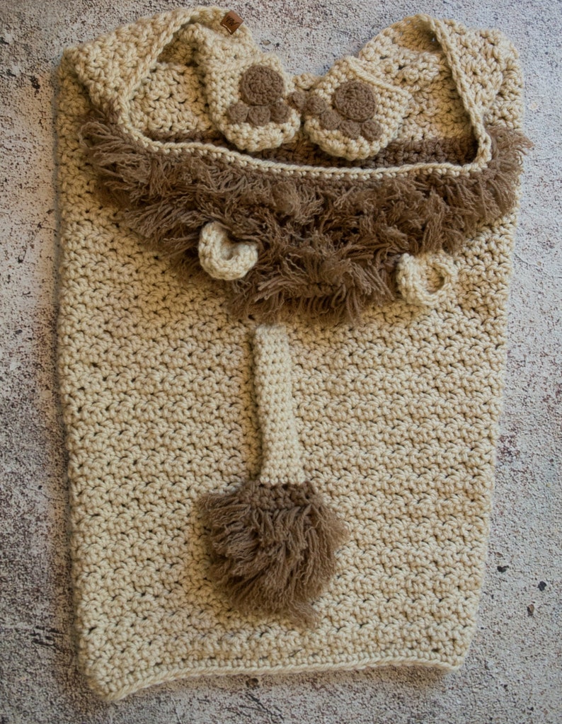 May include: A crocheted lion costume for a baby, featuring a hooded blanket, booties, and a tail with a brown fur trim.