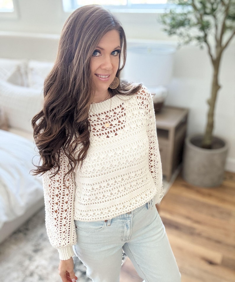 K&ouml;nnte beinhalten: Cremefarbener H&auml;kelpullover mit langen &Auml;rmeln und rundem Ausschnitt. Der Pullover hat ein Lochmuster und wird mit hellblauen Jeans kombiniert. Der Stil ist l&auml;ssig und bequem, geeignet f&uuml;r den Alltag.