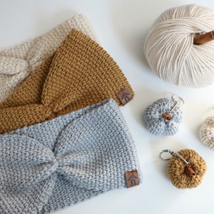 May include: Three knitted headbands in beige, mustard yellow, and gray. The headbands are made with a chunky yarn and have a knotted design. There are also four small knitted pumpkins with cinnamon sticks attached, two in gray and two in mustard yellow.