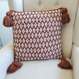 May include: A brown and white geometric patterned throw pillow with brown tassels on each corner.