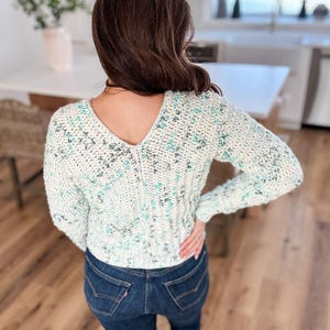 May include: A white and blue crocheted sweater with a V-neck and long sleeves.