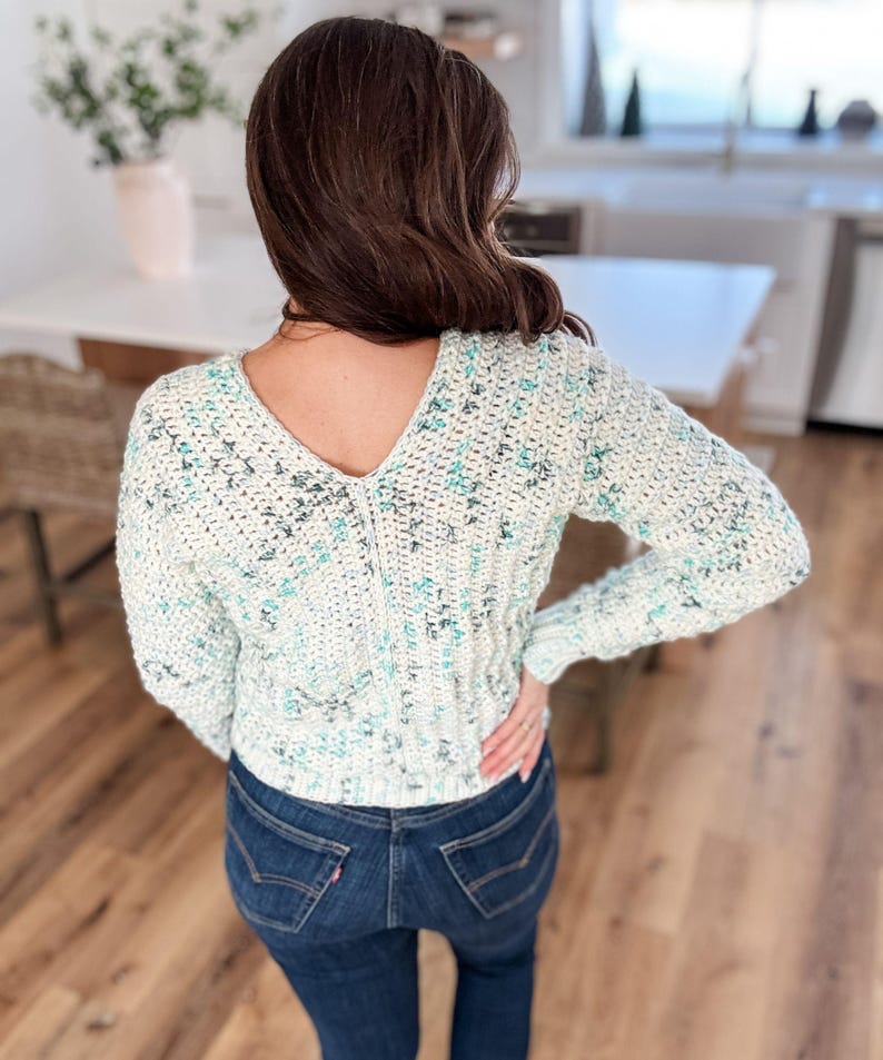 May include: A white and blue crocheted sweater with a V-neck and long sleeves.
